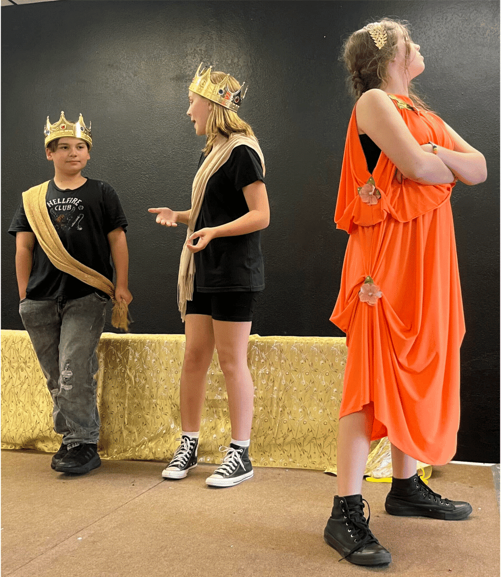 Three teenagers, two with gold crowns and one looking in an orange tunic.